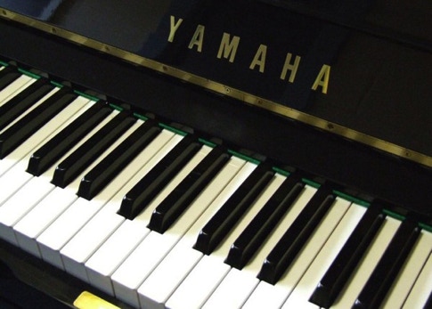 A stylish man in a black suit plays piano in a bar with a woman at the counter, creating a sophisticated atmosphere.